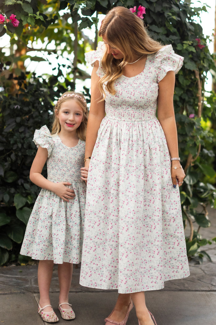 A woman and young girl wear matching Hattie Dress in Pansy Trellis by Ivy City Co, smiling hand-in-hand outdoors amid flowers. The dress is maternity and nursing friendly.