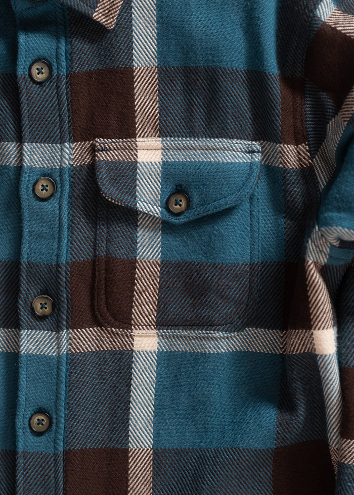 Close-up of a blue, brown, and white plaid flannel shirt with a pocket and buttons, showcasing its textured fabric.