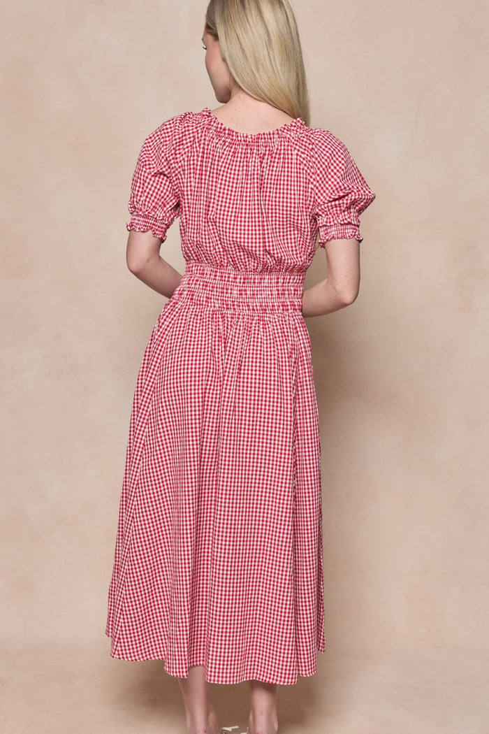 A woman with long blonde hair faces away from the camera, wearing the Ivy City Co Jessie Dress in Red Gingham. This midi dress features puffed short sleeves, a smocked bodice and waist, gathered texture, and is maternity and nursing friendly.