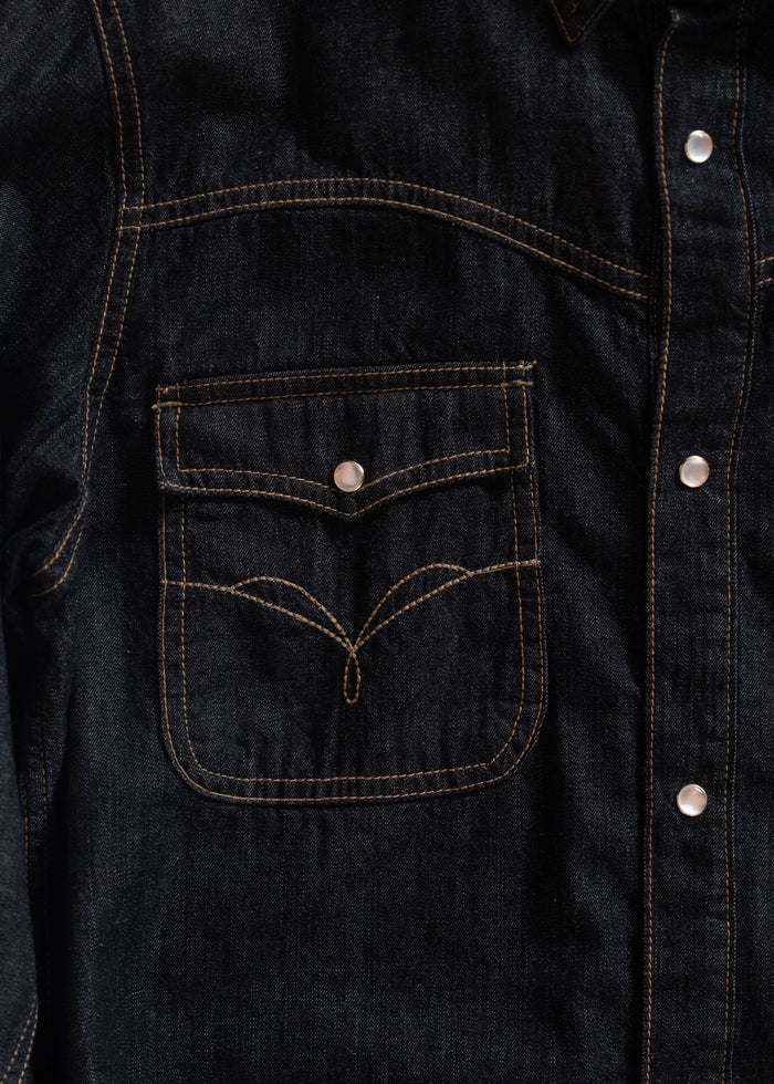 Close-up of a dark denim jacket with contrast stitching and silver buttons, highlighting a front pocket with unique stitching.