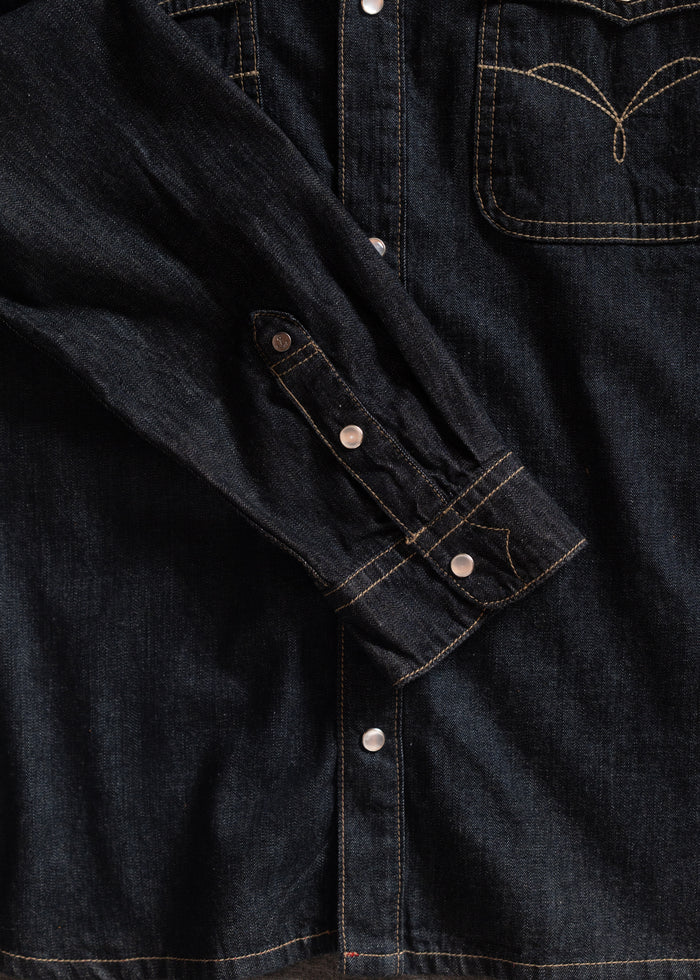 Dark denim jacket with contrast stitching, buttoned cuffs, and a chest pocket. The fabric has a classic, rugged texture.