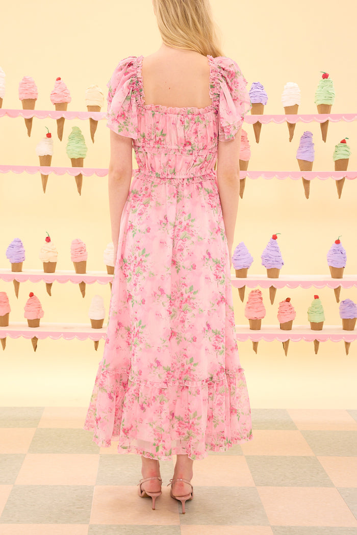 Woman wearing a pink floral dress standing in front of an ice cream cone pattern.