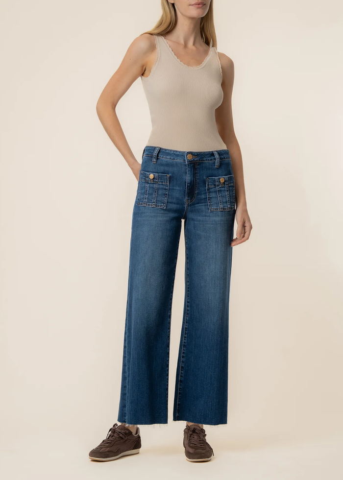 Woman wearing dark blue wide leg jeans with a tan tank top and brown sneakers