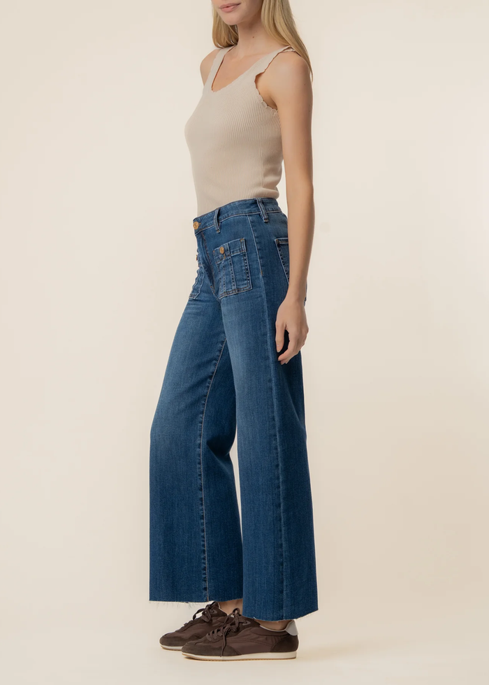 Woman wearing dark blue wide leg jeans with a tan tank top and brown sneakers