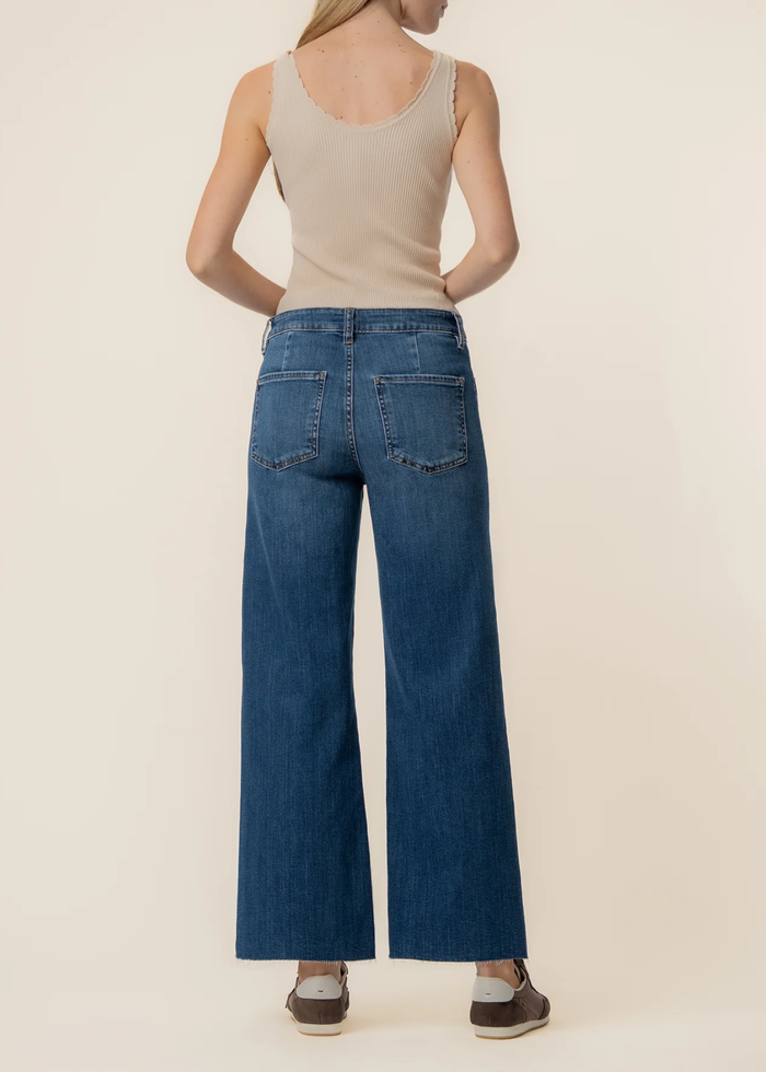 Woman turned around wearing dark blue wide leg jeans with a tan tank top and brown sneakers