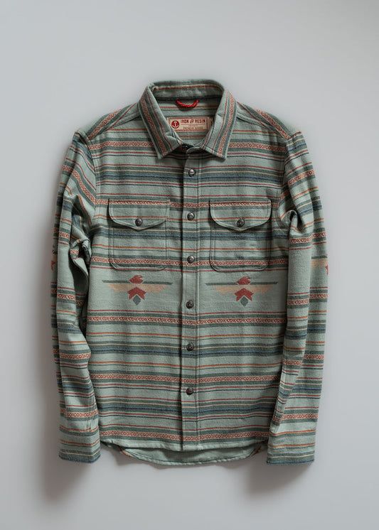 Striped green flannel shirt with buttoned pockets, featuring geometric patterns, displayed on a light gray background.