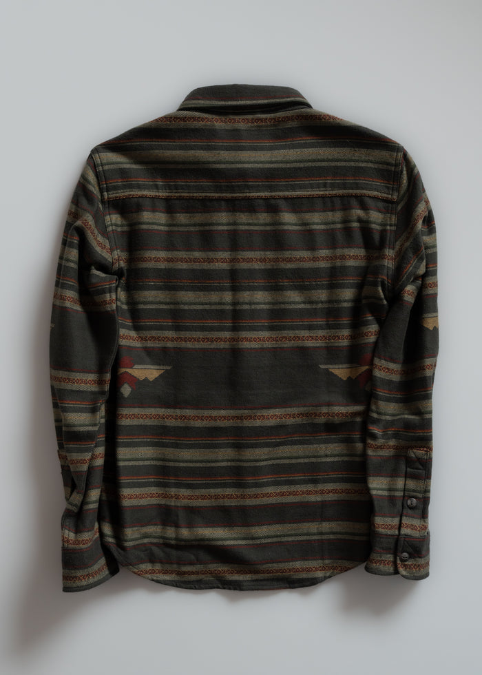 Back view of a long-sleeve shirt with green, brown, and red horizontal stripes and geometric patterns on a plain background.