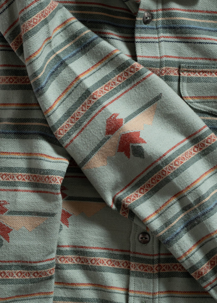 Close-up of a patterned shirt with green, red, and beige stripes and geometric designs, highlighting its texture and buttons.