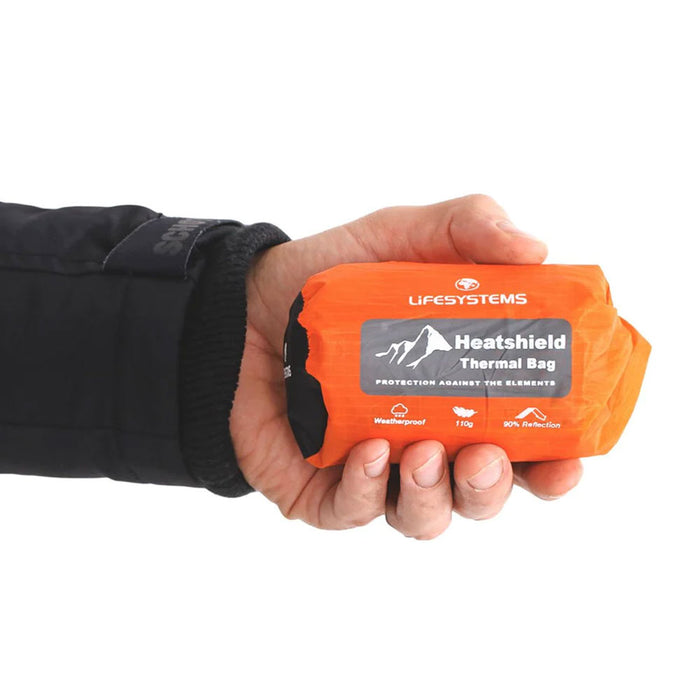 Studio shot on a white background of Lifesystems Heatshield Bivi Bag packed in its stuff sack being held in a persons hand