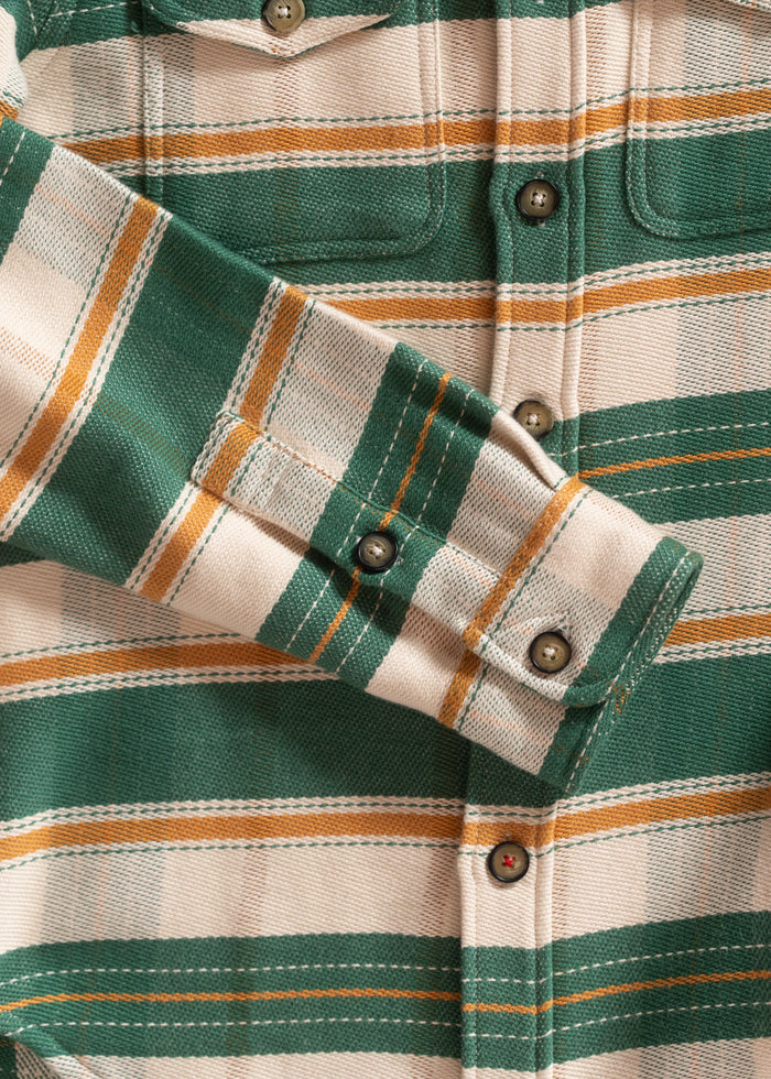 Green and beige plaid shirt with orange stripes, buttoned cuffs, and chest pocket, showcasing detailed stitching and texture.