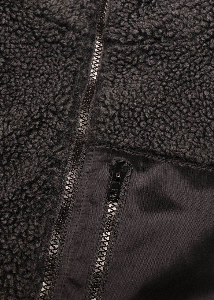 Close-up of a black fleece jacket with a visible zipper and textured fabric, highlighting its cozy and warm material.