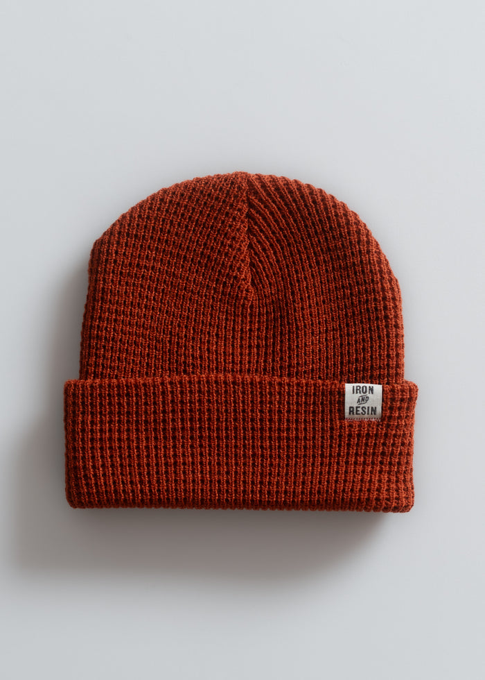 Rust-colored knit beanie with "Iron and Resin" label on the cuff, displayed on a light gray background.