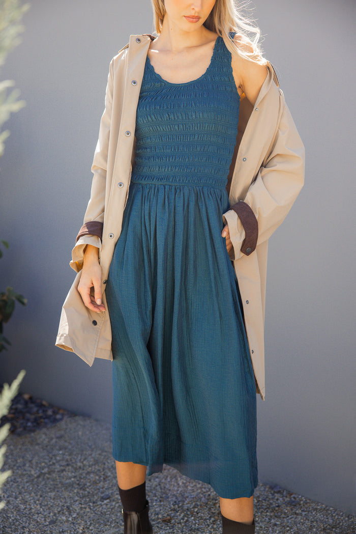Woman wearing a blue dress and beige coat against a gray background