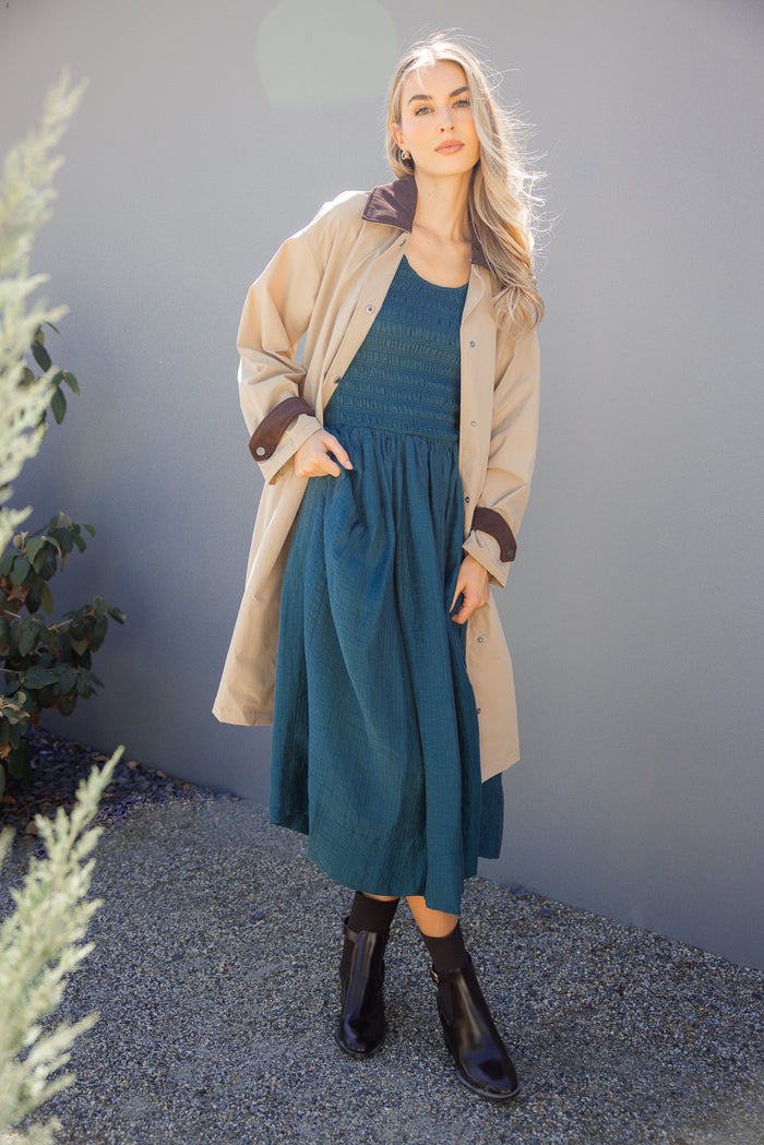 Woman wearing a teal dress and beige cardigan against a gray wall.