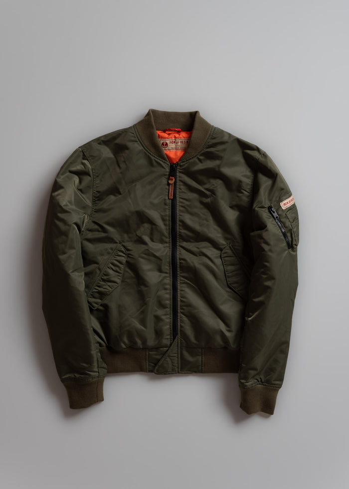 Olive green bomber jacket with orange lining, front zipper, and sleeve pocket, displayed on a gray background.