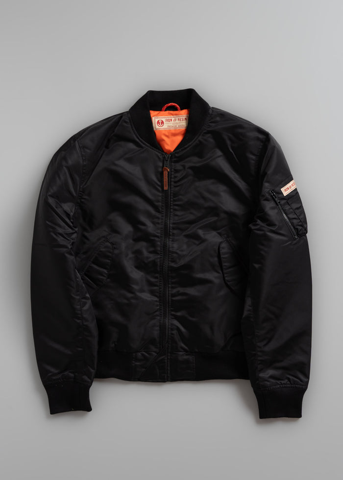 Black bomber jacket with orange lining and zip pocket on sleeve, displayed on a gray background.