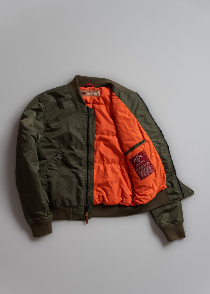 Olive green bomber jacket with bright orange lining, unzipped to show interior label and pocket, laid flat on a light surface.