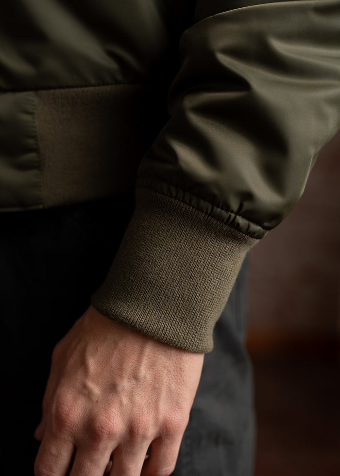 A close-up of a hand in a green jacket with ribbed cuffs, highlighting the texture and detail against a blurred background.