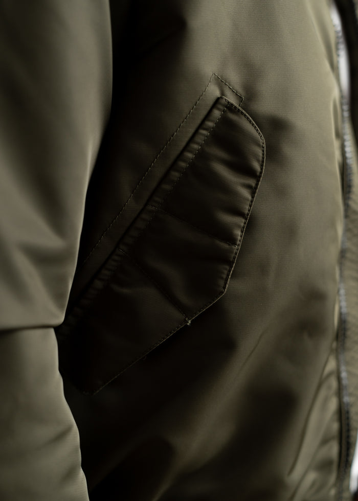 Close-up of a green jacket pocket, showcasing detailed stitching and smooth fabric texture, highlighting its quality design.