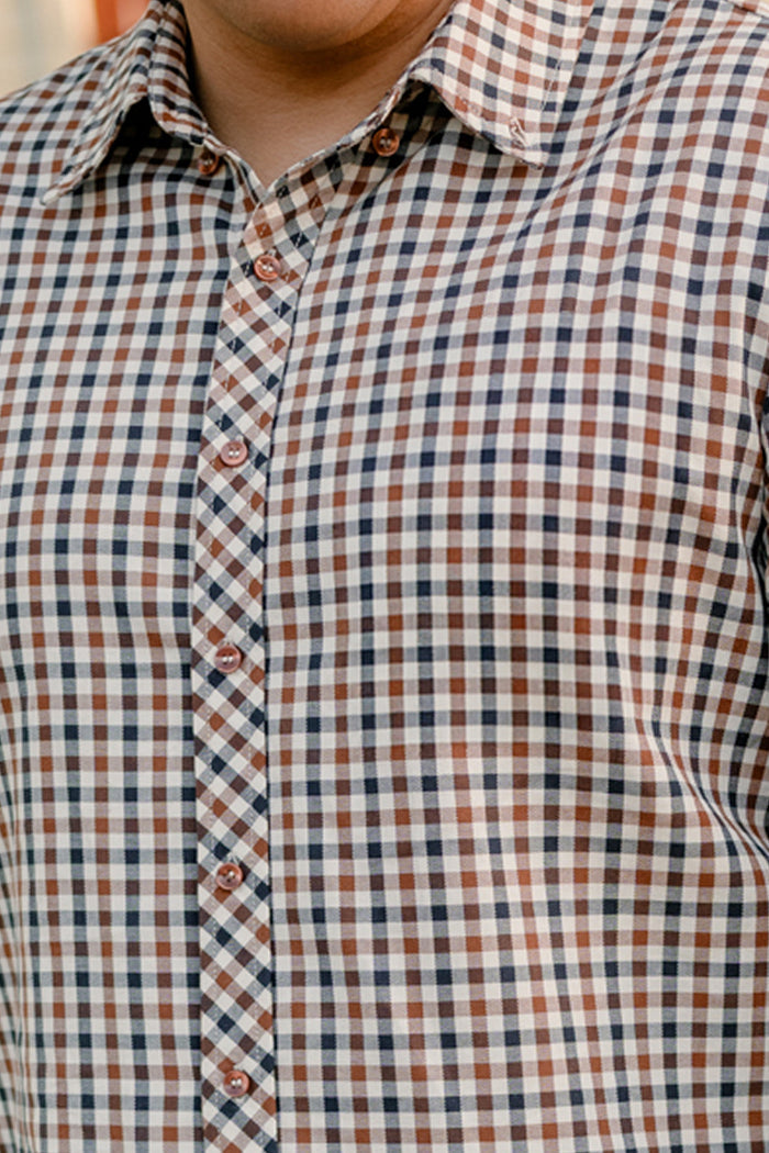 A person wearing the Ivy City Co Mens James Shirt in Chestnut Gingham—a brown, black, and white checked cotton shirt ideal for fall layering. Only the torso and part of the neck are visible.