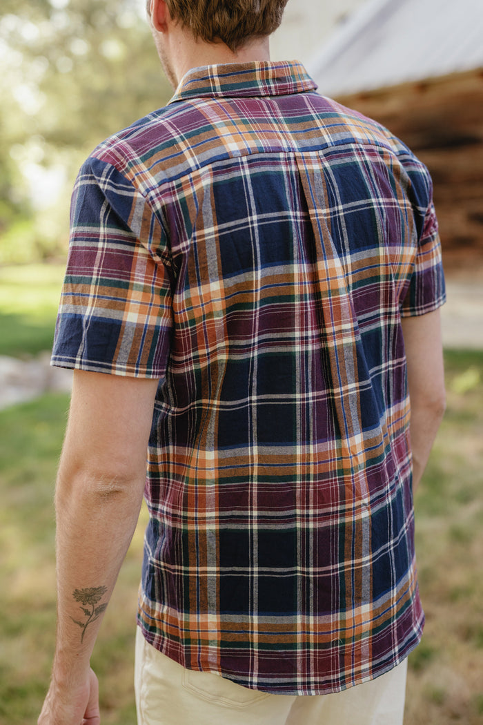 A person wearing the Mens James Shirt in Midnight Plaid by Ivy City Co, paired with light pants, stands outdoors with their back to the camera—an effortless look perfect for any fall wardrobe.