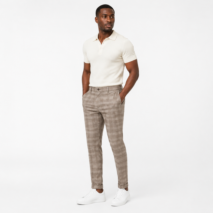Khaki plaid trousers on an adult Black male model in a three-quarter studio view with a cream polo and simple white sneakers.