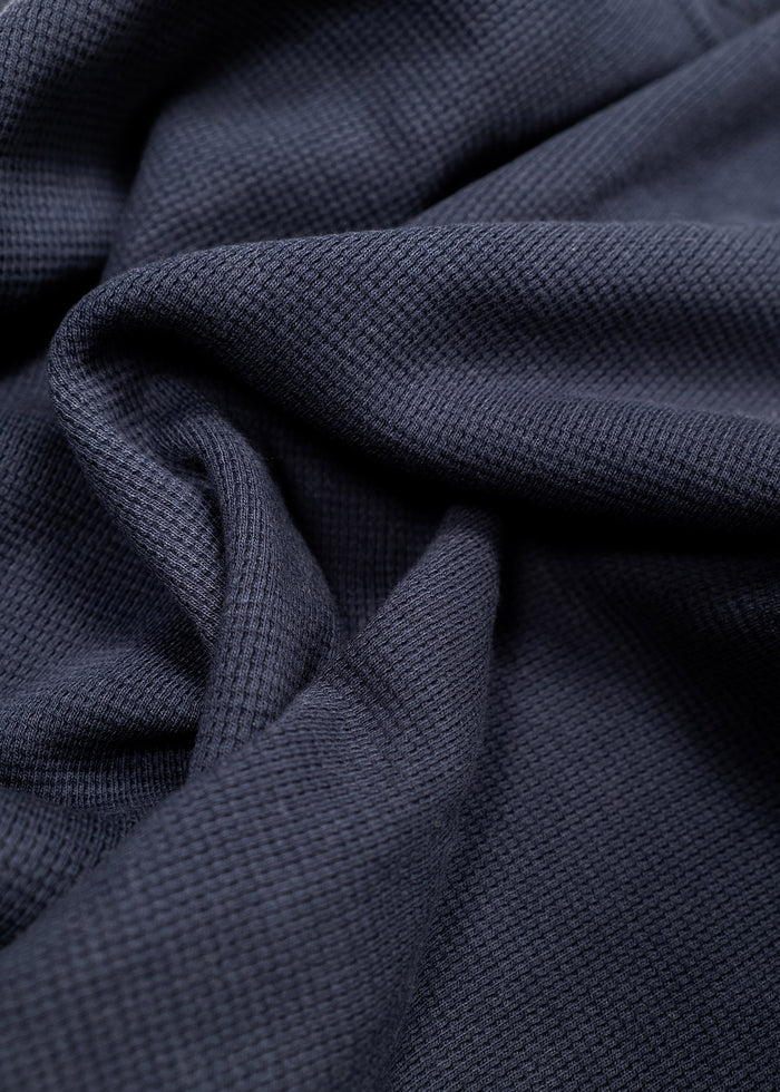 Close-up of dark blue textured fabric with soft folds, showcasing its intricate weave and smooth surface.