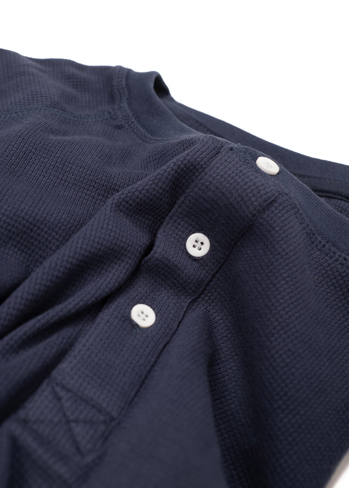 Close-up of a navy blue waffle-knit shirt with white buttons, showcasing texture and detail in the fabric and stitching.