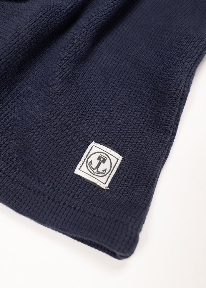 Navy knit fabric with a stitched white anchor logo patch on the corner, showcasing a maritime theme and textured design.