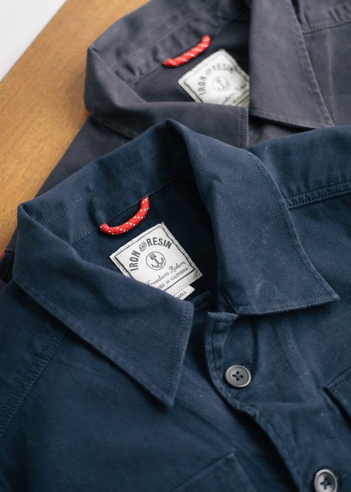 Two navy shirts with red loop details and Iron & Resin labels lie on a wooden surface, showcasing their classic design.