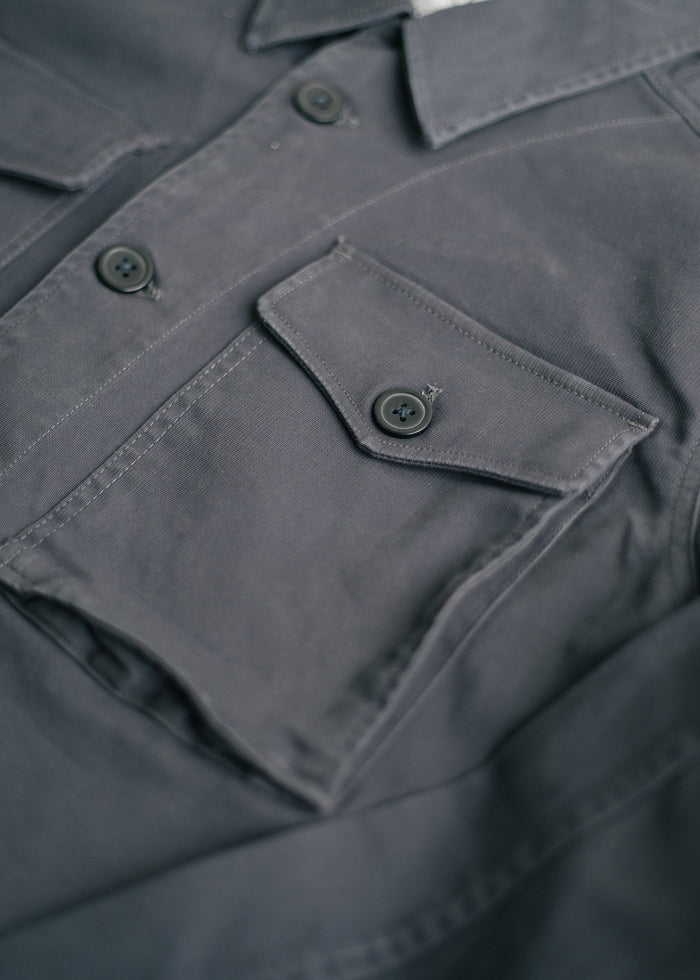 Close-up of a gray shirt with buttoned flap pockets and a collar, highlighting the fabric texture and stitching details.