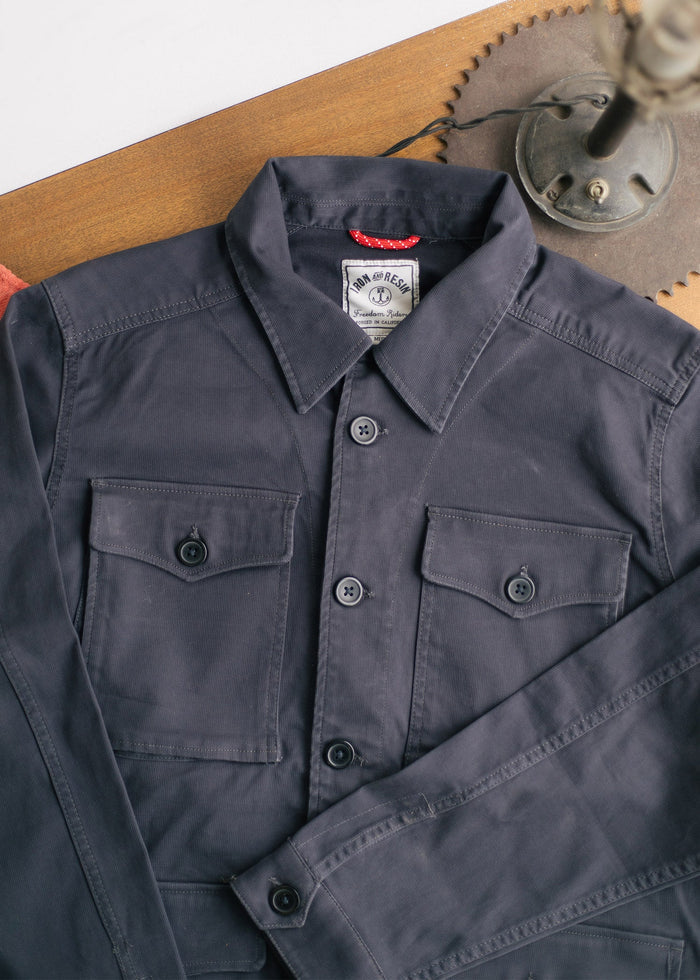Dark blue button-up shirt with two chest pockets, laid on a wooden table beside a vintage lamp.