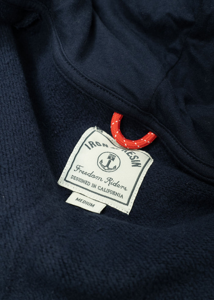 Navy blue fabric with a label reading "Iron & Resin, Freedom Riders, Designed in California, Medium" and a red loop detail.