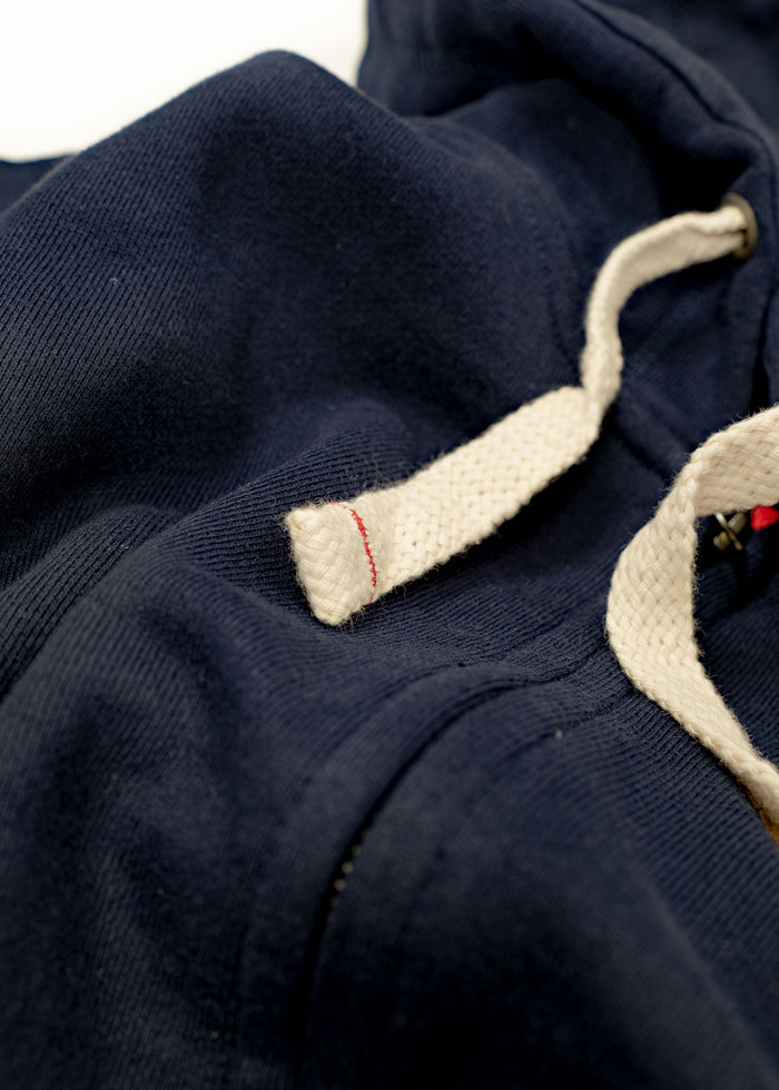 Close-up of a navy hoodie with white drawstrings and visible stitching detail, highlighting texture and craftsmanship.