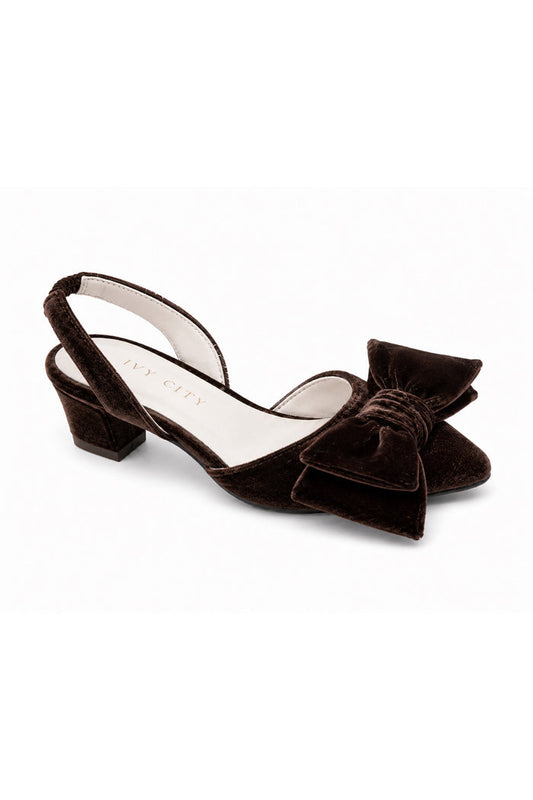 The Mini Eloise Bow Heel in Brown by Ivy City Co is a single dark brown velvet slingback shoe with a low block heel and a large matching bow on the closed toe, featuring a supple leather lining for added comfort, displayed on a white background.