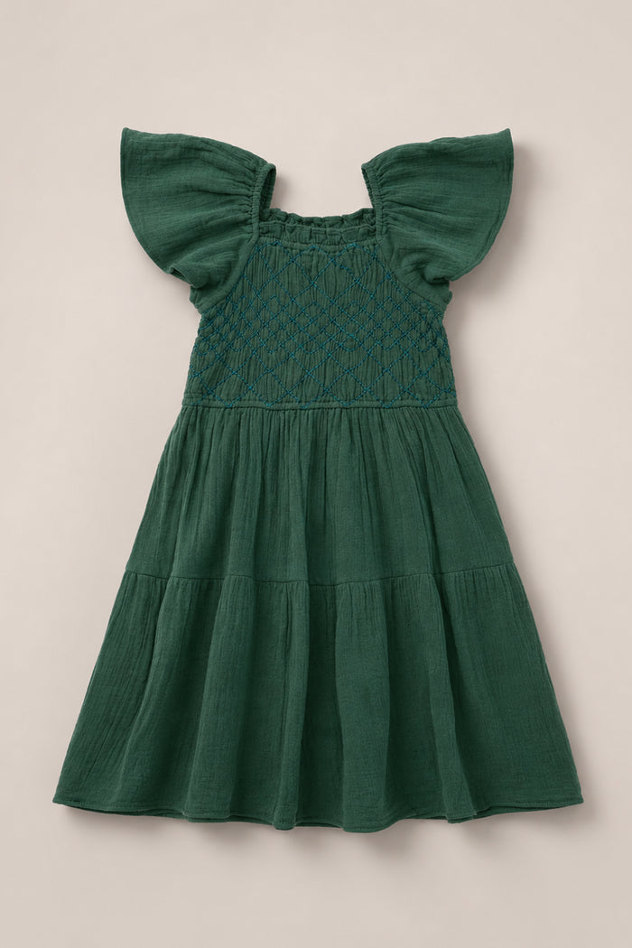 The Mini Jade Dress in Evergreen by Ivy City Co is a green girls’ dress with flutter sleeves and a smocked bodice accented by delicate blue stitching. Featuring a tiered, flowy skirt, the dress is displayed flat on a neutral background, offering a charming blend of comfort and style.