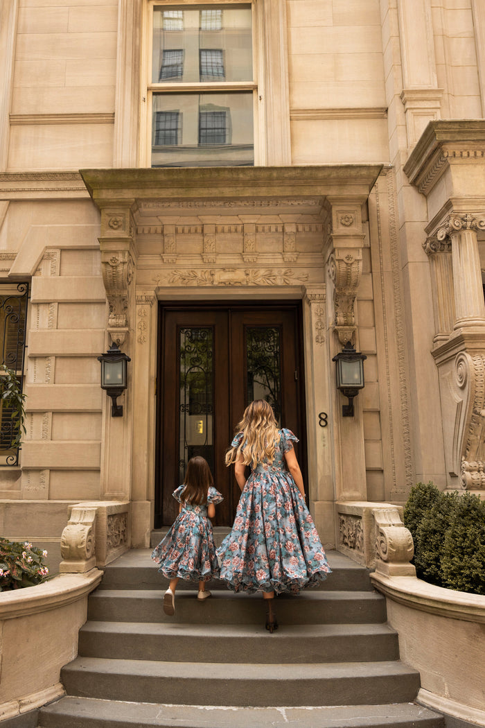 A woman and a young girl, both dressed in matching Ivy City Co Mini Lisette Dresses in Rose Dusk, ascend the steps to a grand building with double wooden doors—embodying the elegance of a fall wedding.