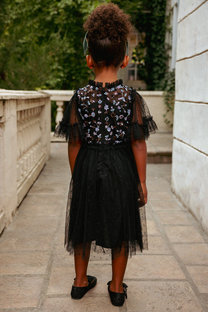 Person wearing a black floral dress with sheer sleeves in an outdoor setting.
