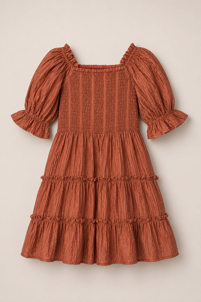 The Mini Madeline Dress in Apple Cider by Ivy City Co, featuring puff sleeves, a smocked bodice, and three ruffled tiers on the skirt, is displayed flat on a light beige background.