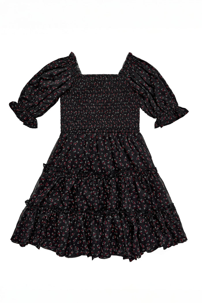 The Mini Madeline Dress in Black Ditsy Floral by Ivy City Co is a short-sleeved, black mini dress featuring a smocked bodice, puffed sleeves, and a tiered ruffle skirt. This charming dress is adorned with a small ditsy floral print in red and white.