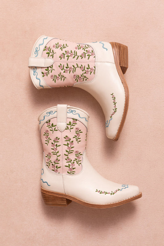 Two Mini Rosemary Cowgirl Boots in Cream & Pink by Ivy City Co, featuring wooden heels, floral embroidery, and delicate pink trim, are placed on a soft pink background.