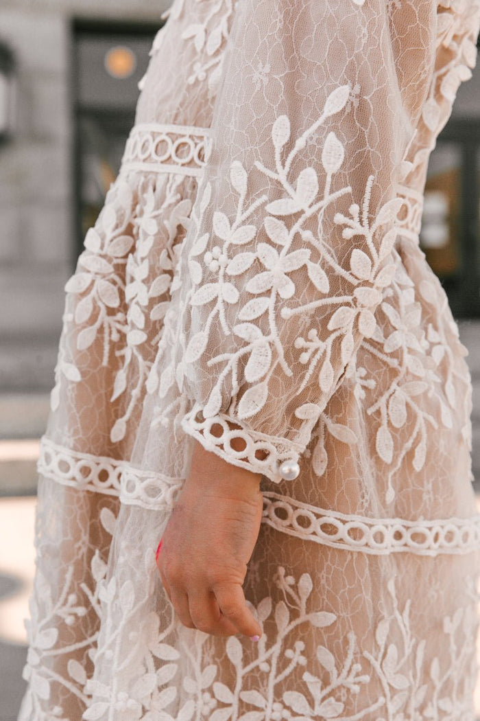 Close-up of a person wearing the Ivy City Co Mini Sicily Dress with Long Sleeves, featuring white lace, floral embroidery, and decorative circular trim. Focus is on the sleeve and side as the person’s hand rests by their side.