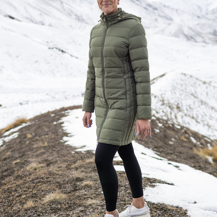 Woman wearing Moke - Sydney Cloud Touch 90/10 Down Coat (SYDNEY) in the colour Olive Green on a hill with snow in the background.
