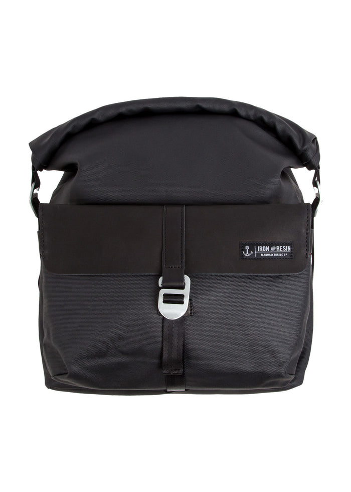 Black Iron and Resin messenger bag with a roll-top design and metal buckle, featuring a front logo patch on a smooth surface.