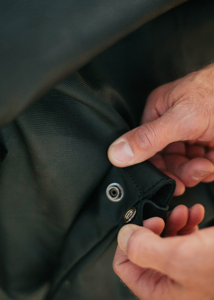 Hands fastening a metal snap button on a textured black fabric, focusing on the detail and craftsmanship of the material.