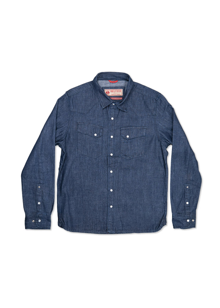 Blue denim shirt with white buttons, two chest pockets, and a collar, laid flat on a white background.