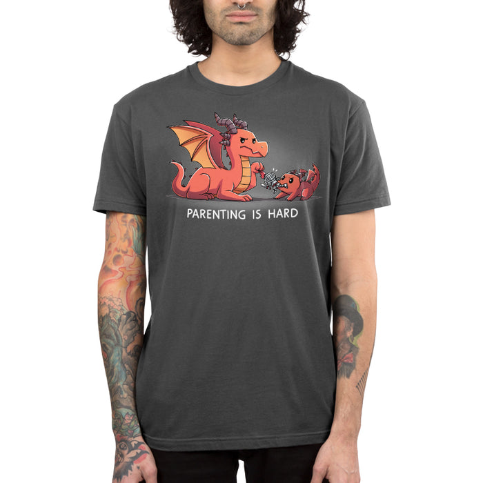 Premium Cotton T-shirt_TeeTurtle charcoal gray Parenting is Hard apparel featuring a parent dragon holding onto a toy knight while its baby dragon grabs it with its mouth.