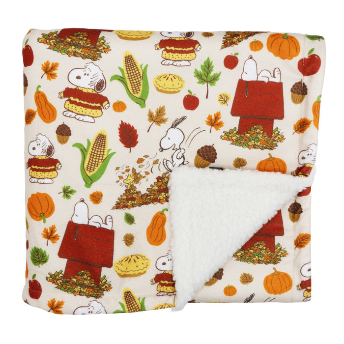 The Sassy Woof Pet Blanket - Peanuts™ Harvest features a cozy fall design with Snoopy, leaves, corn, apples, pumpkins, and pies on a cream background. Its plush white sherpa lining adds extra warmth for your pet.