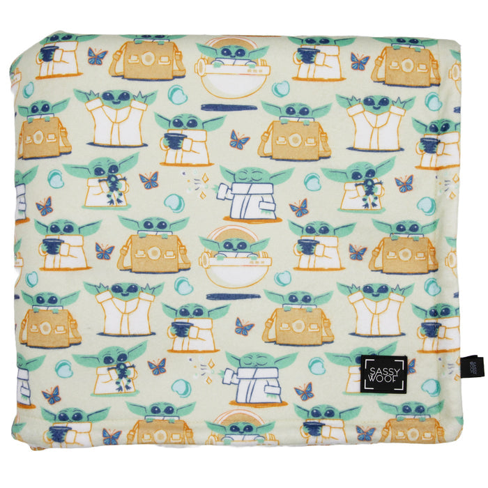The Sassy Woof Pet Blanket - STAR WARS™ The Child™ features a soft, folded microfiber design with cartoon Baby Yoda, robots, and butterflies on light green. A black tag with the Sassy Woof logo decorates the corner. Inspired by Lucasfilm’s iconic character.