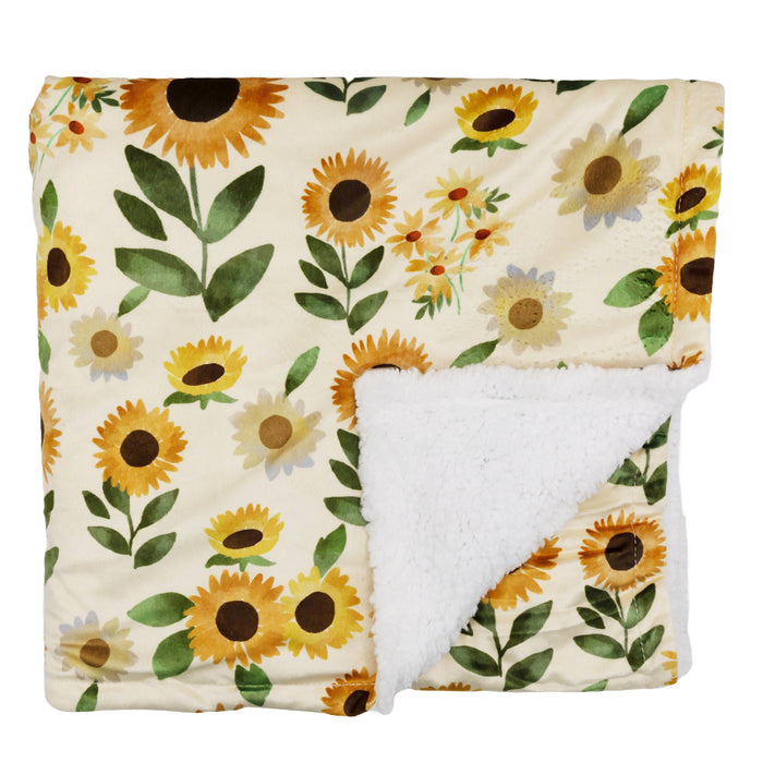 The Sassy Woof Pet Blanket - Sunflower Dreams features a sunflower pattern on a cream background, shown folded with one corner turned up to reveal its soft, white, fluffy lining.